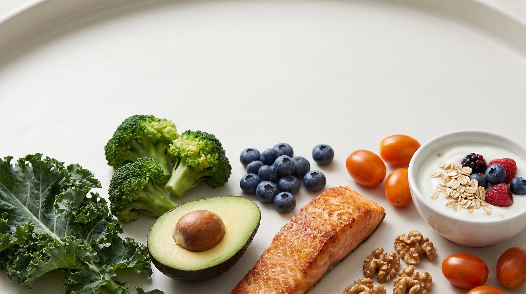 A spread of fresh whole foods — kale, broccoli, avocado, salmon, blueberries, and Greek yogurt
